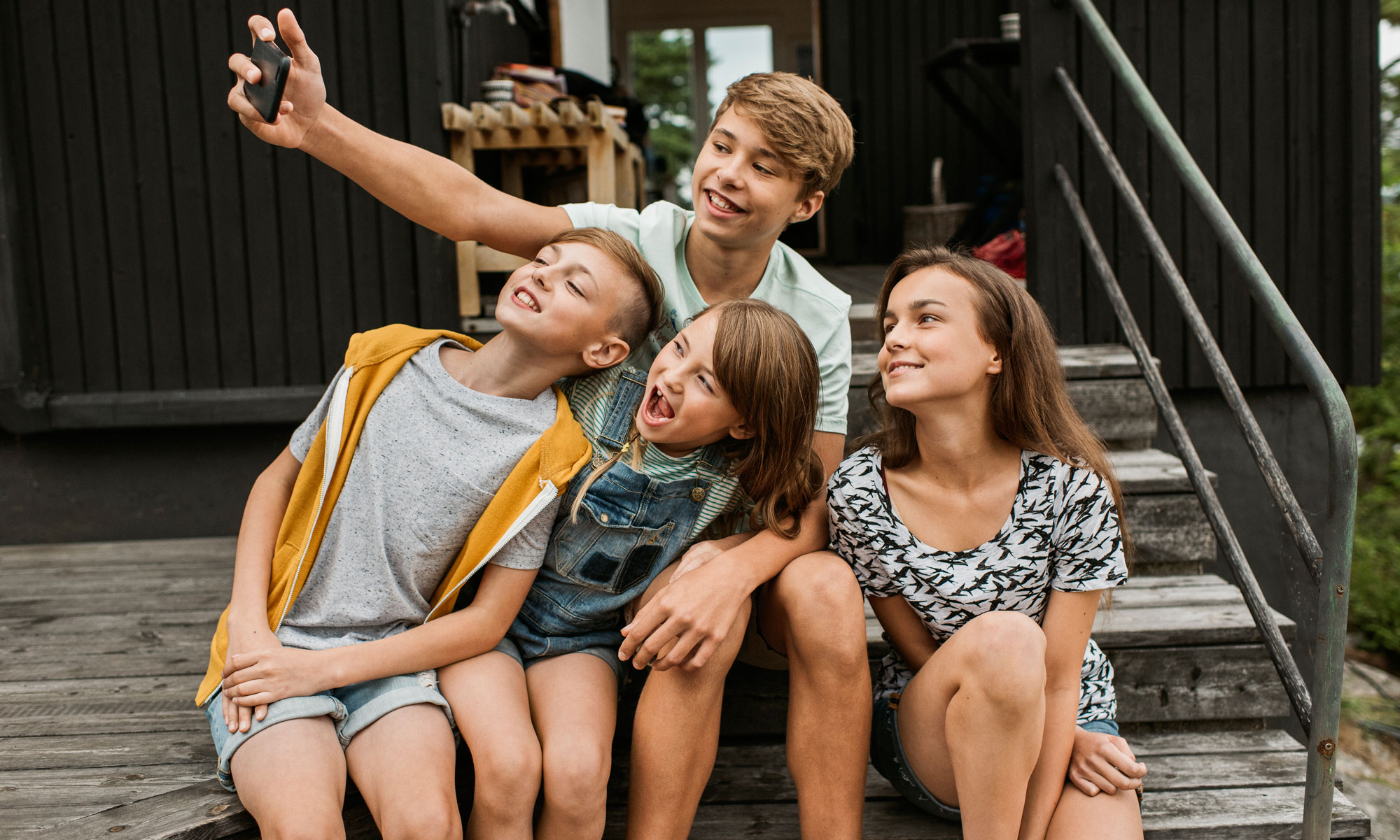Fyra glada barn tar en grupp selfie ute på trappan